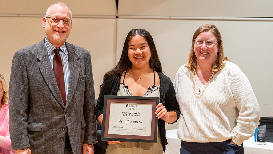 Student poses with their award, alongside Dean and Department Chair for a photo.