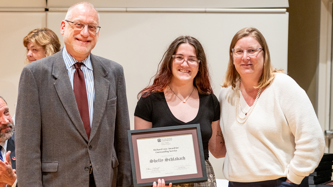 Student poses with their award, alongside Dean and Department Chair for a photo.