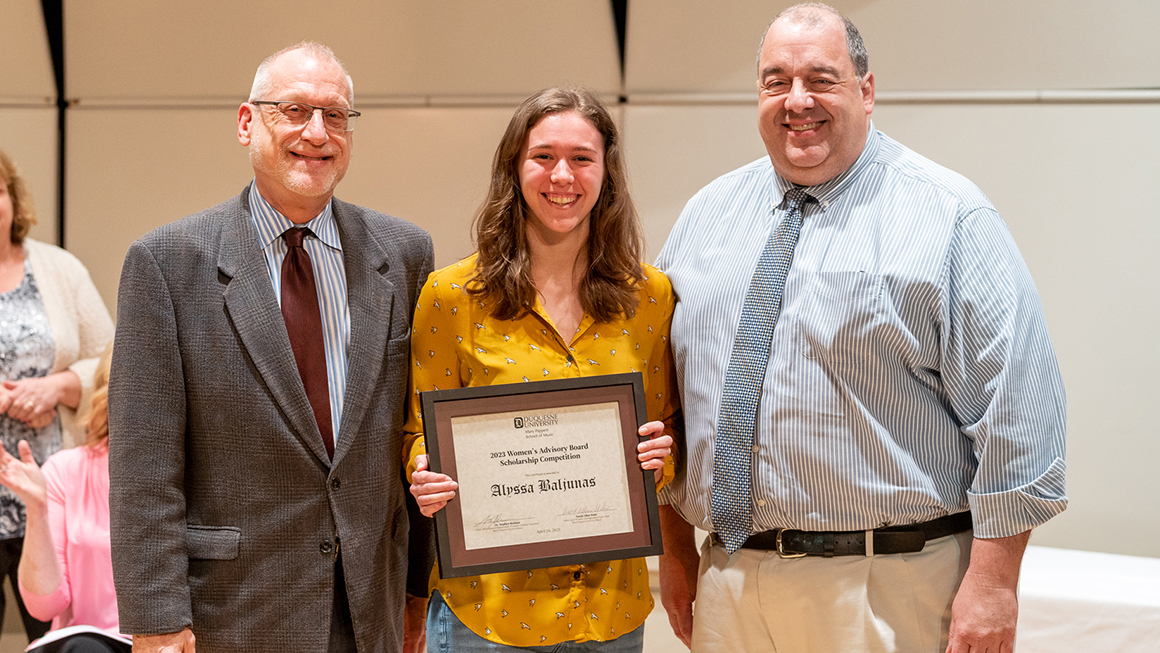 Student poses with their award, alongside Dean and Department Chair for a photo.