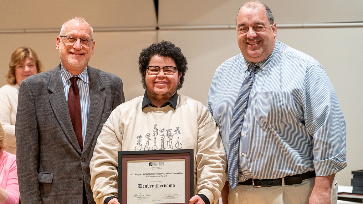Student poses with their award, alongside Dean and Department Chair for a photo.