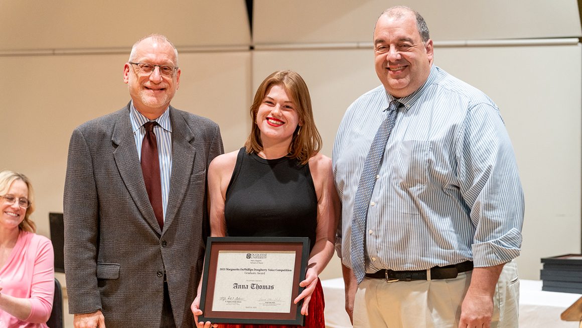 Student poses with their award, alongside Dean and Department Chair for a photo.