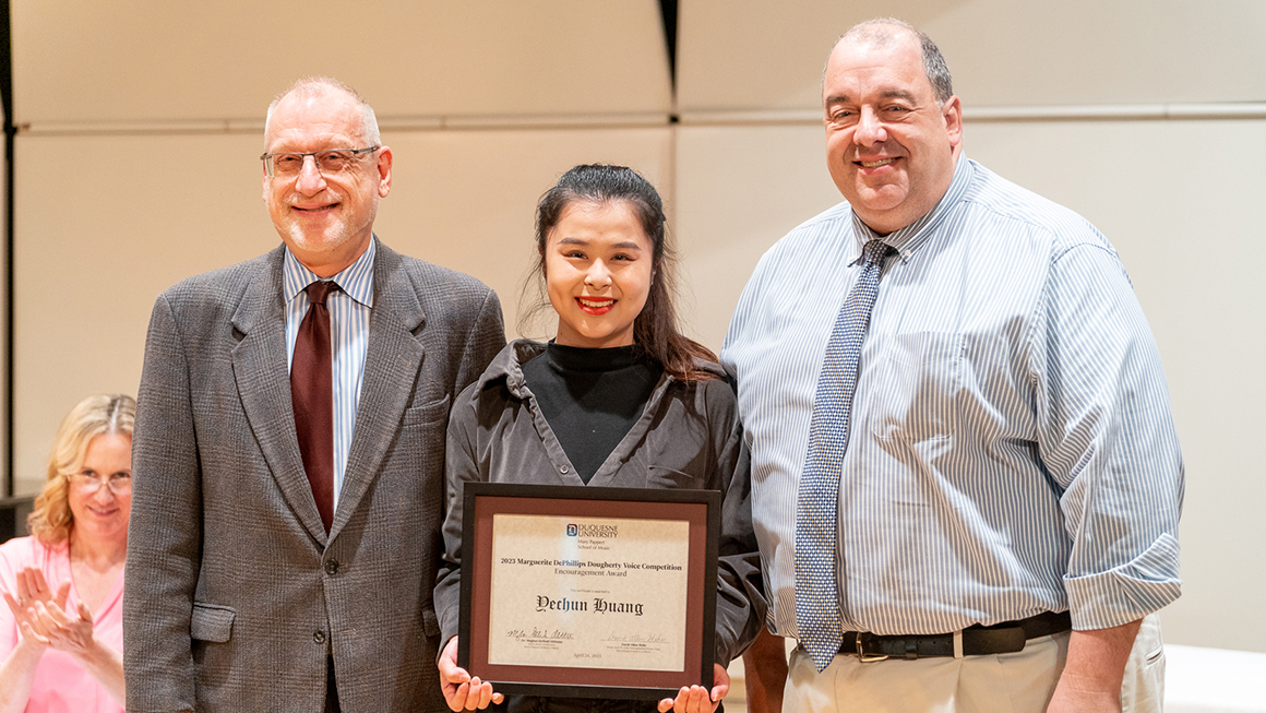 Student poses with their award, alongside Dean and Department Chair for a photo.