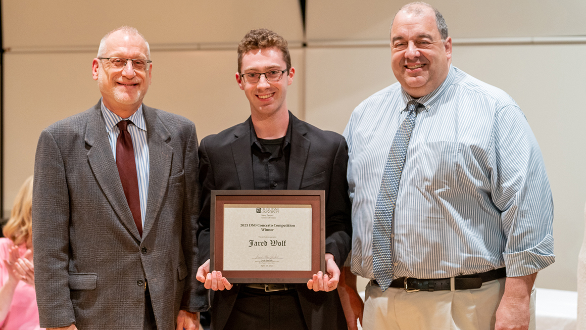 Student poses with their award, alongside Dean and Department Chair for a photo.