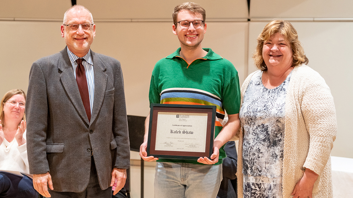 Student poses with their award, alongside Dean and Department Chair for a photo.