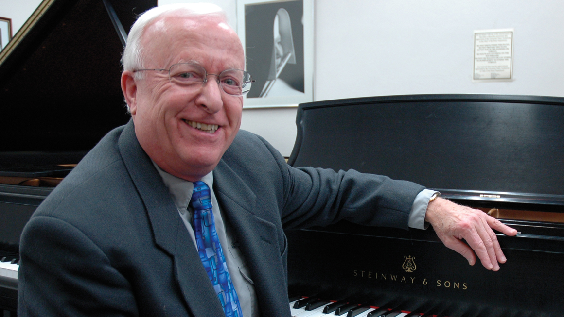 A man poses for a photo at a piano.