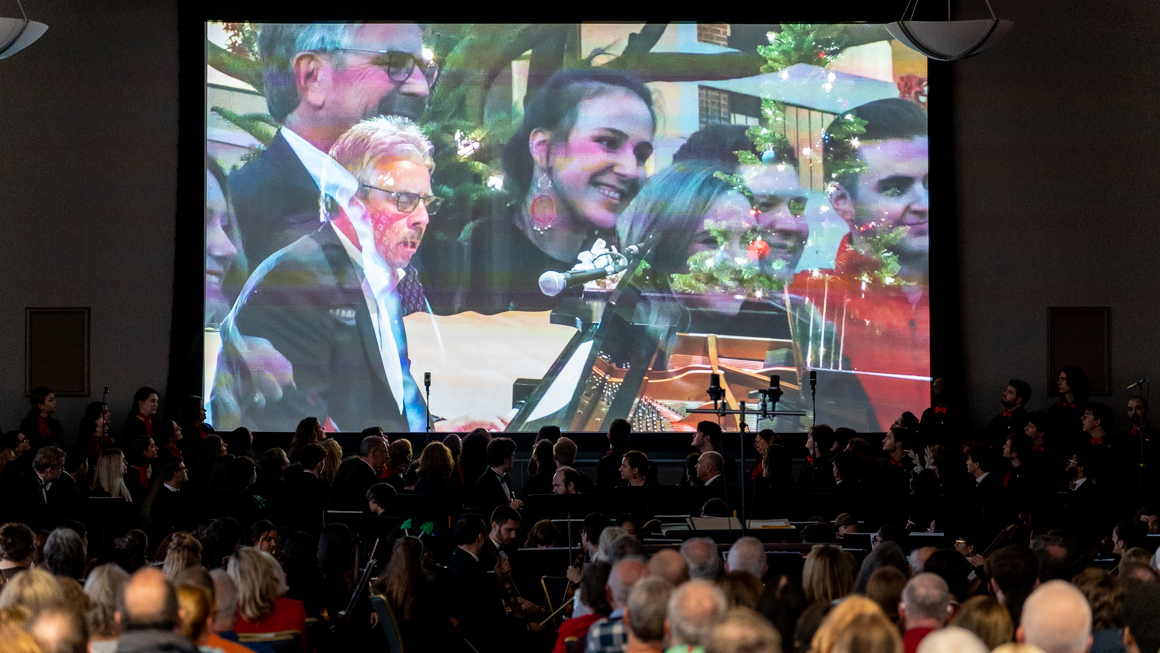 An audience watches a video projected on a screen.