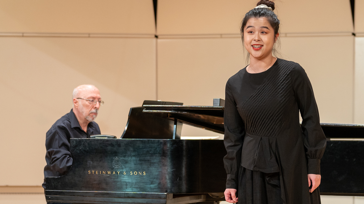 A student performs on stage with a pianist.