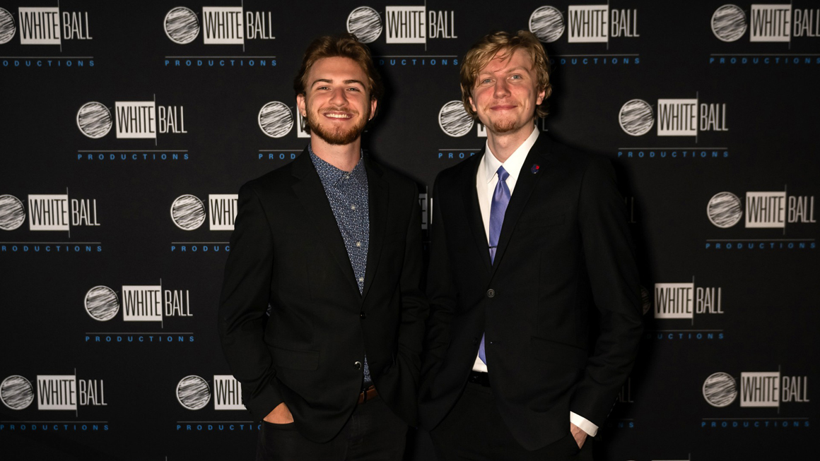 Two people pose for a photo in front of a logo wall.