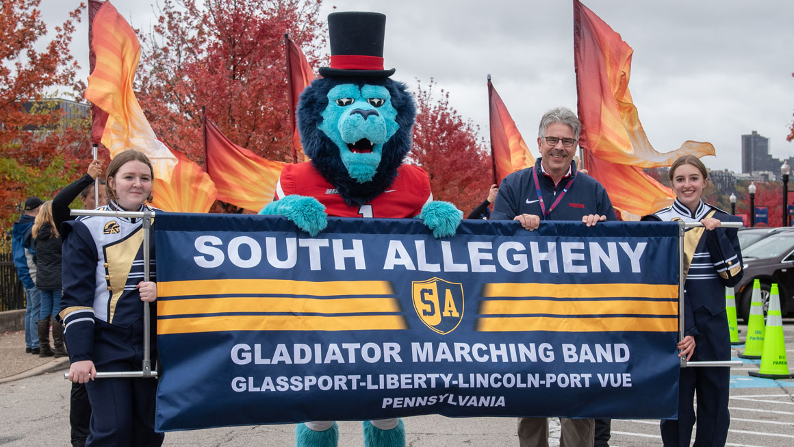 Band members, along with the Duquesne Duke and President Ken Gormley hold the South Allegheny Marching Band sign.