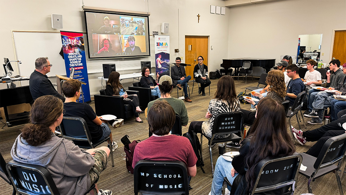 A group of music tech alumni, including some on a projected Zoom call, speak to current music tech students.