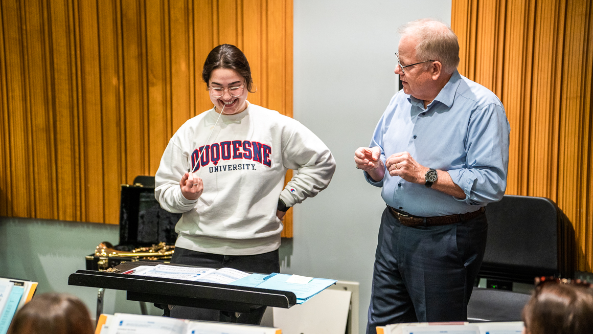 A faculty member works with a student on their conducting skills.
