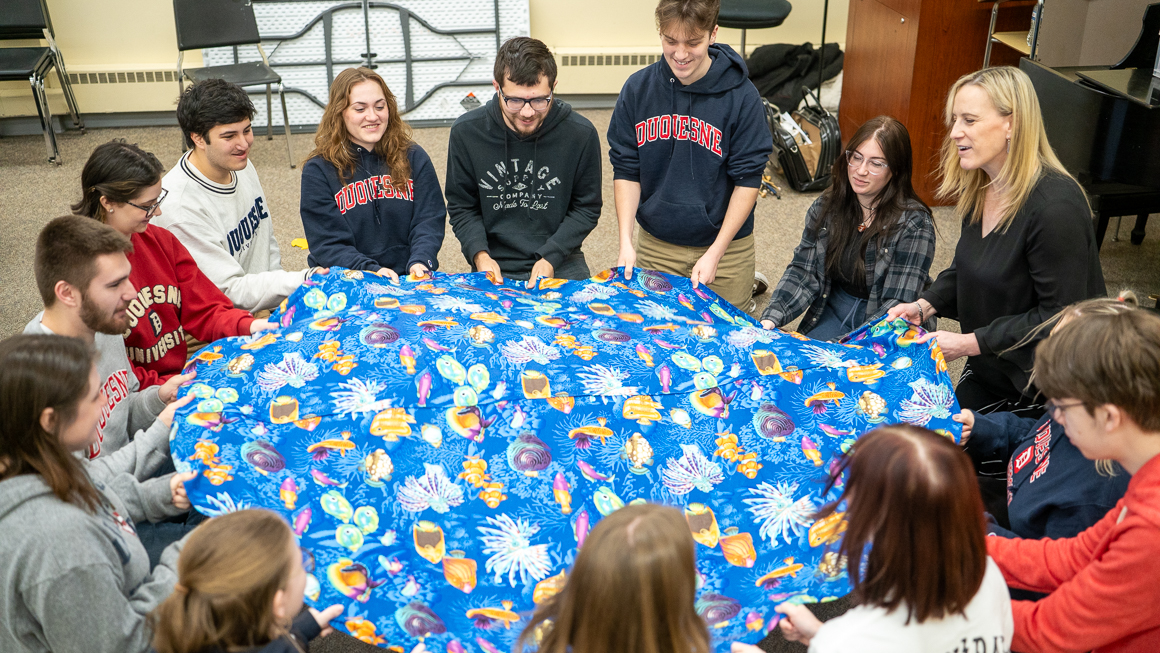 Students learning about early childhood music education by singing and playing with a parachute.