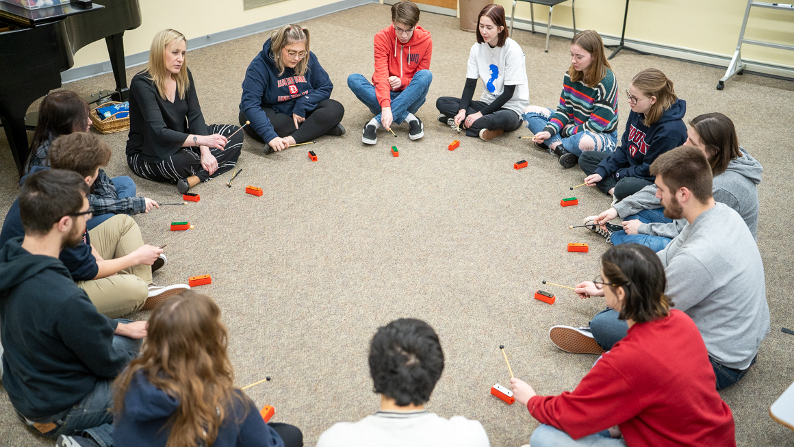 Faculty member demonstrates a children's instrument to a class seated in a circle.