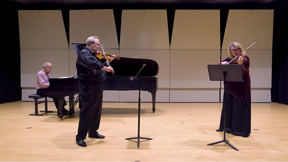 Two violinists play on stage with a pianist.