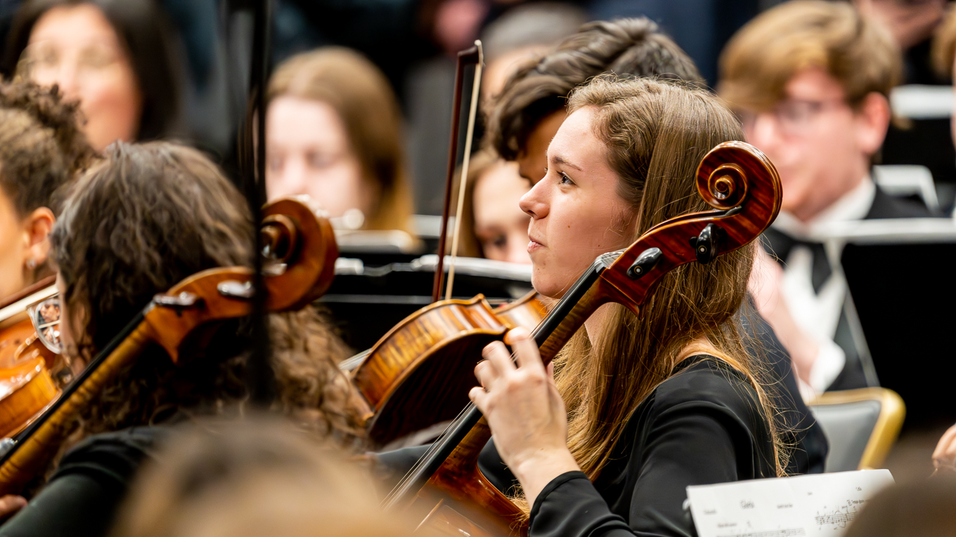 A cellist performing amongst other string players.