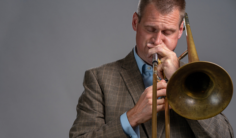 A person wearing a brown suit plays a trombone.