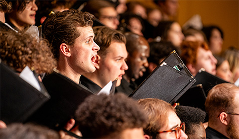 A choir performs on stage. One specific student is the center of focus, while the rest fall into the background.