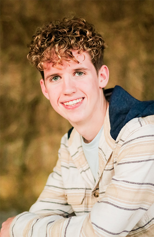 A person with curly hair leans on a tabletop and poses for a photo in front of a blurry background.