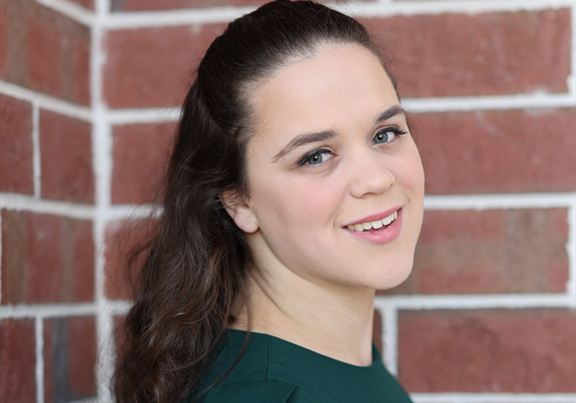 A woman poses in front of a brick wall.