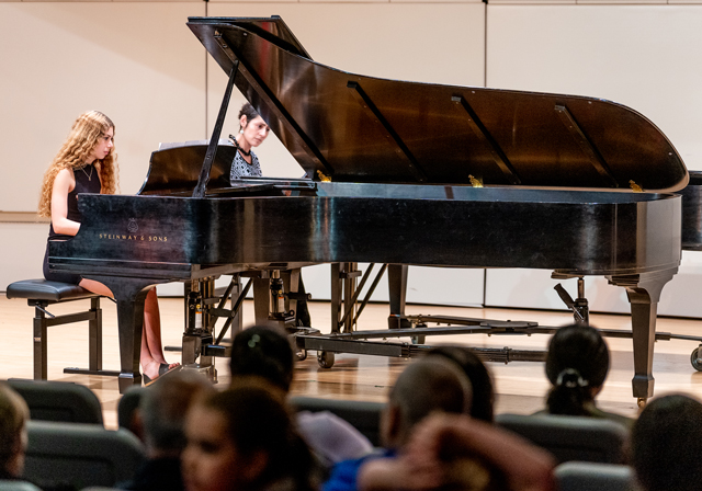 A student and their teacher perform on pianos.