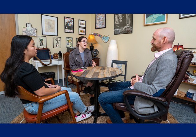 Three people sitting around a table smiling and talking.