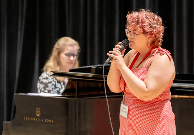 A person sings with a pianist in the background.
