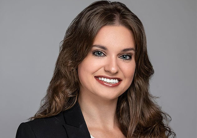 A woman poses in professional attire for a photo.