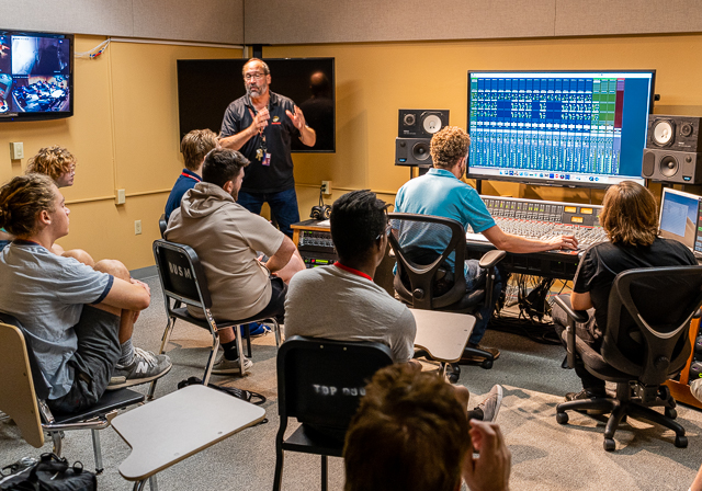 A professor works with students in a music technology lab.