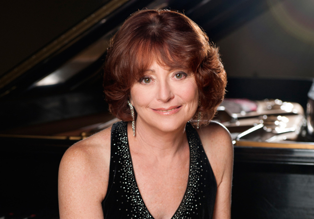 A person wearing a gown smiles in front of a piano.