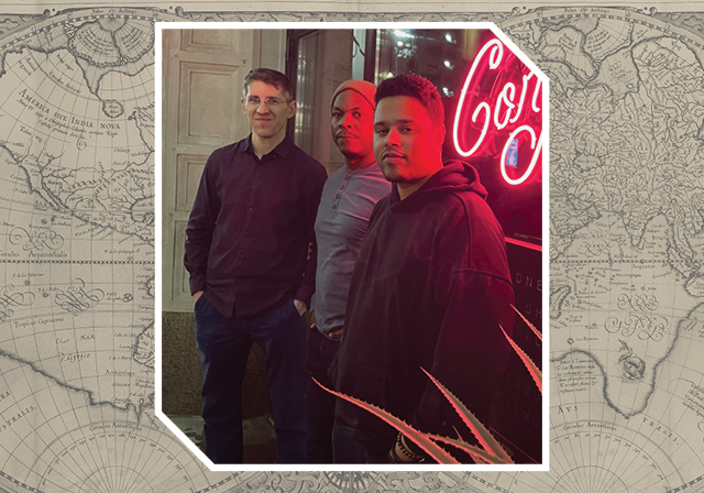 Three people pose for a photo in the glow of a red neon light. The image is overlaid on top of a faded historic world map.