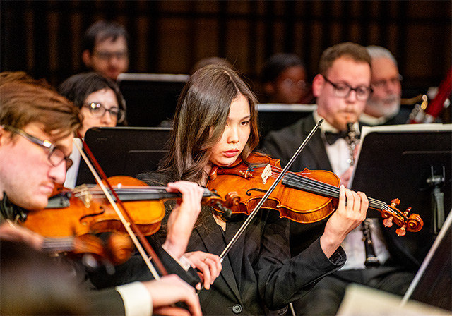 Violinists wearing all black concert attire perform on stage.
