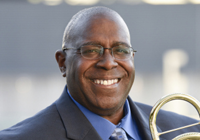 A person with a trombone smiles for a portrait.