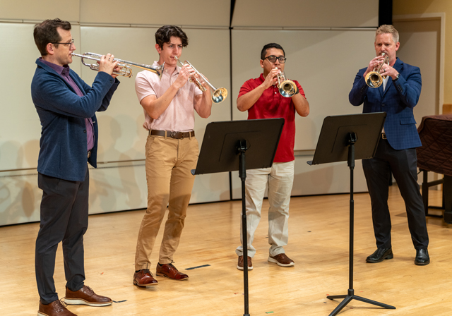 Four people play trumpets on stage.