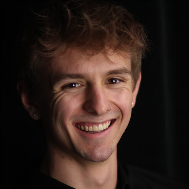 Boy smiles in front of dark background.