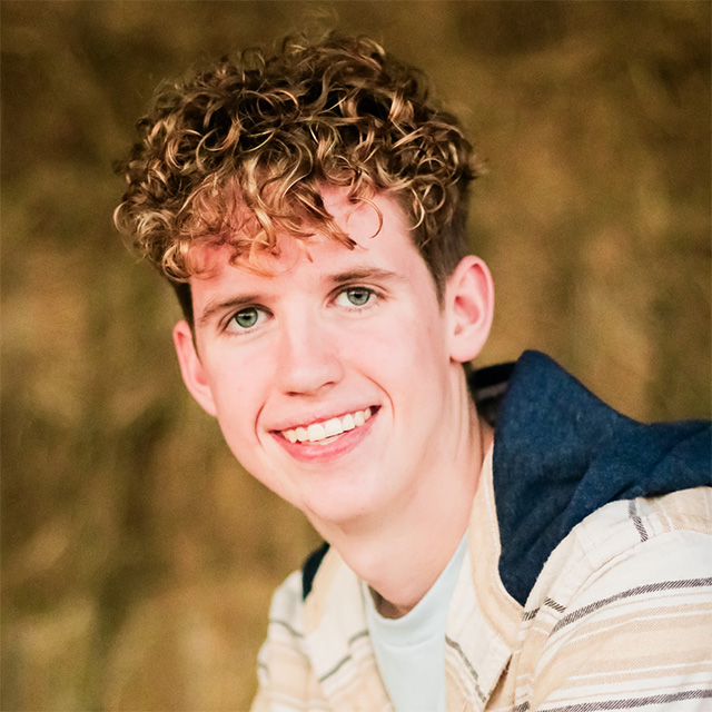 Boy smiles in a wooded area.