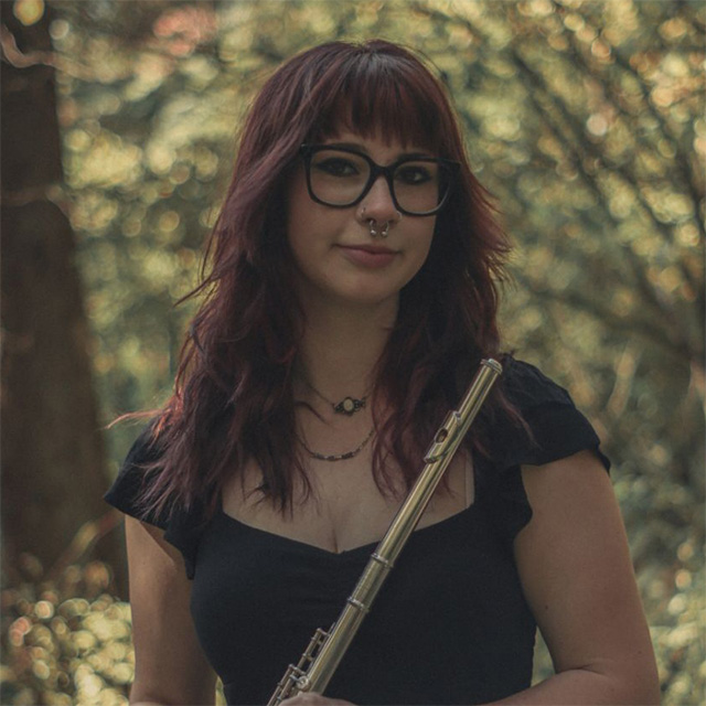 Young woman holds flute in front a green tree.