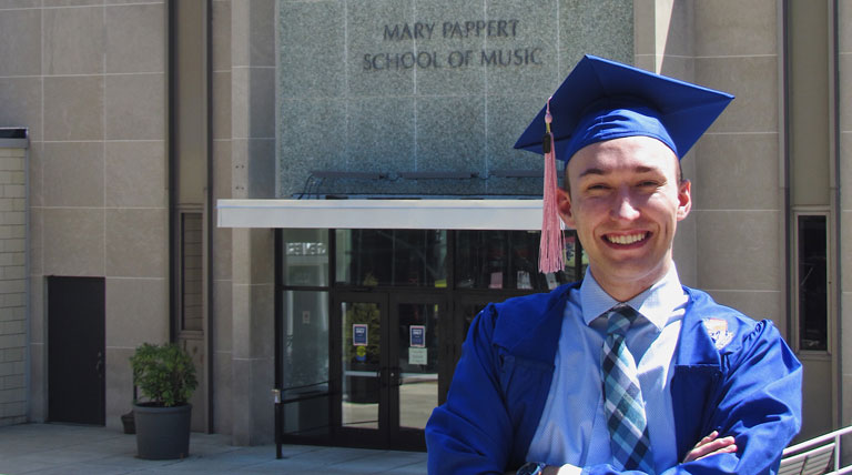 Blake Mechtel poses in cap and gown in front of the Mary Pappert School of Music.