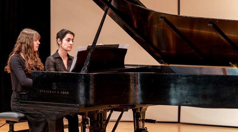 A student and a professor perform at a piano.