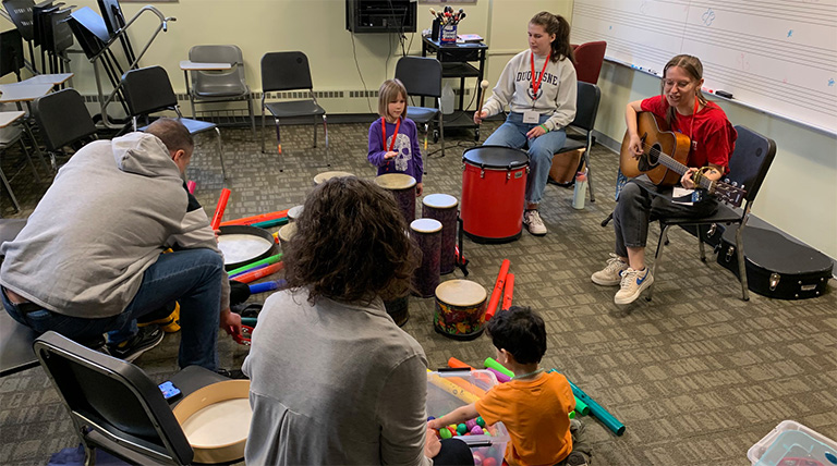 Six people sit in a circle with various percussion equipment.
