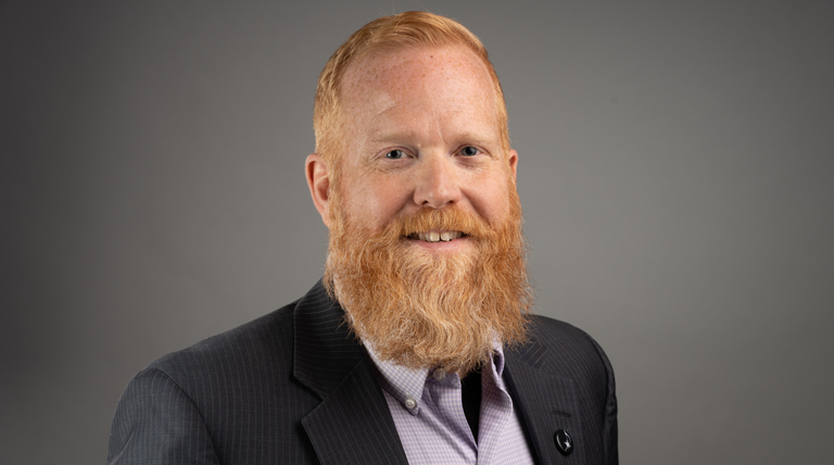 Todd Goodman poses for a headshot in front of a gray background.