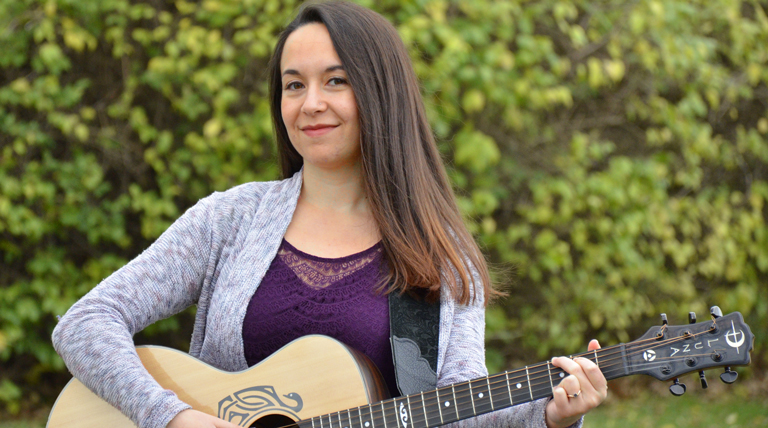 Meghan Roche poses outdoors with a guitar.