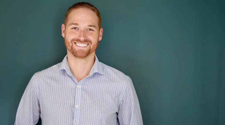 Phillip Mauskapf poses for a headshot in front of a teal background.