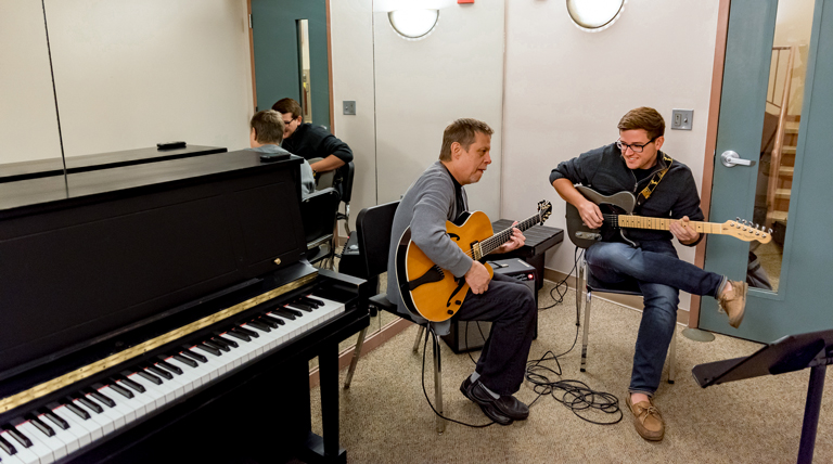Two guitarists work in a practice room.