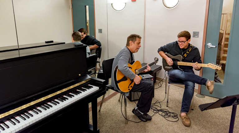 A student takes a guitar lesson with a teacher.