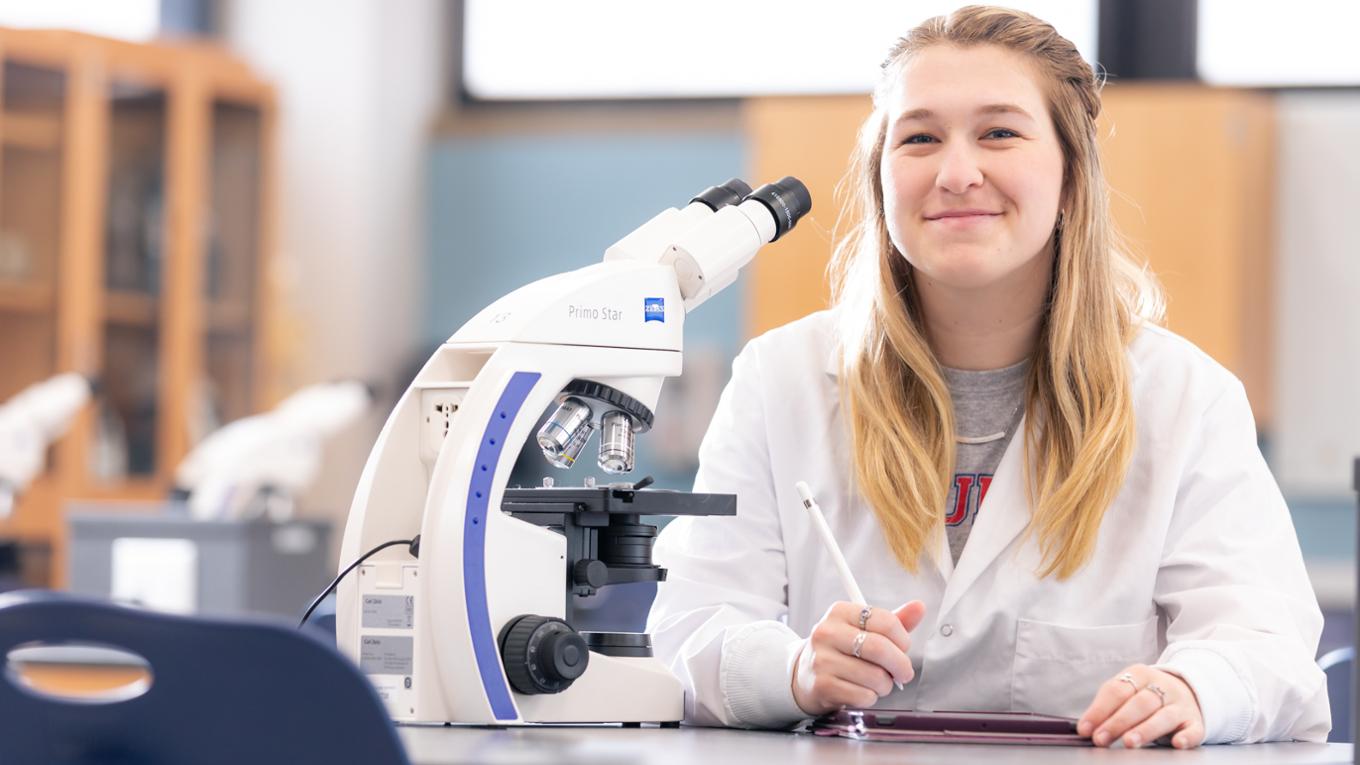 student with a microscope smiling at camera