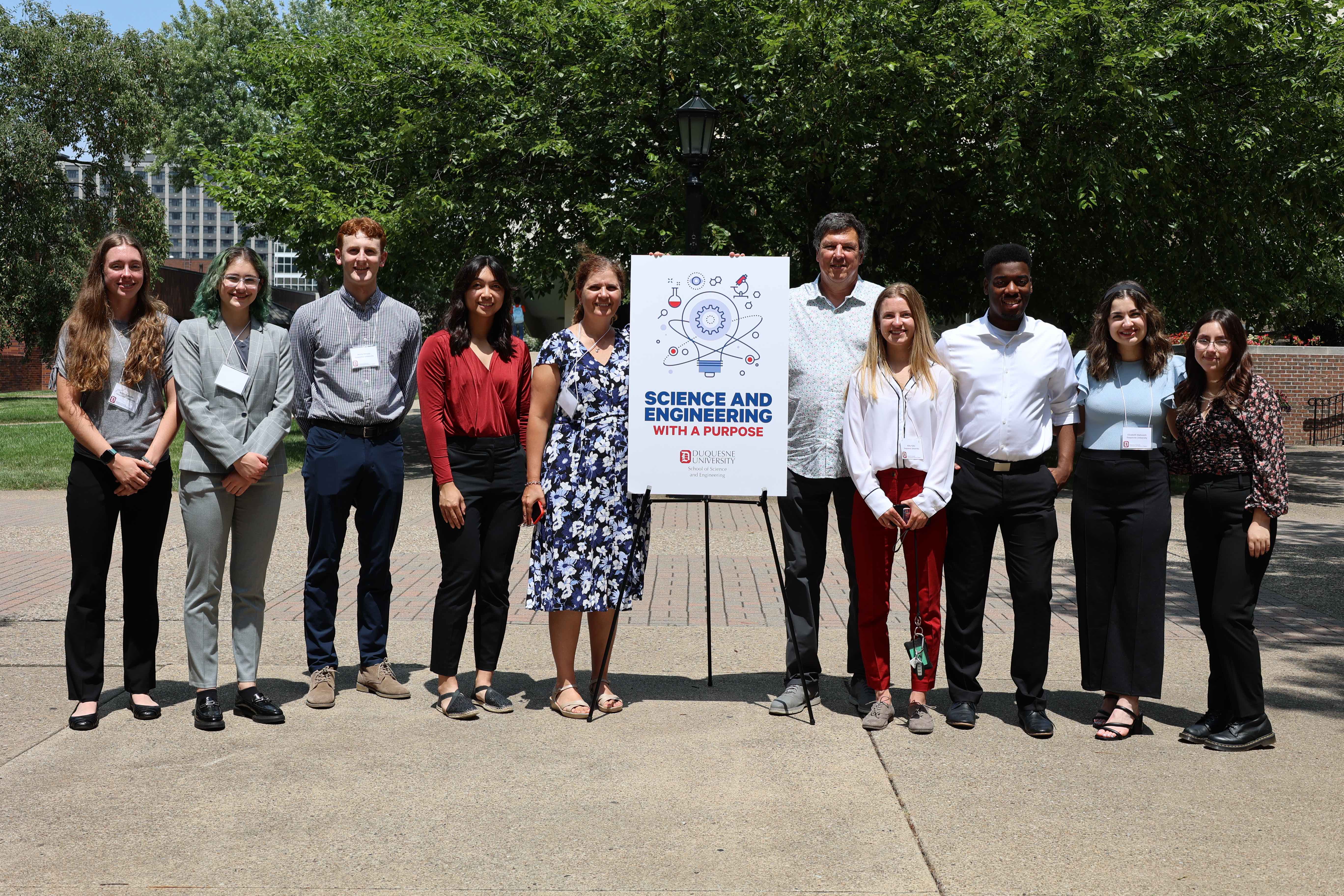 undergraduate research program students and faculty standing beside a sign that says "Science and engineering with a purpose"