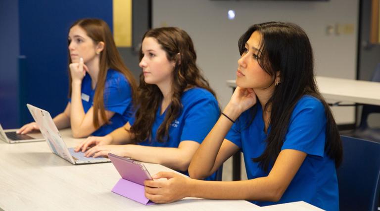 Two nursing students sit at a table, engaged in discussion. 