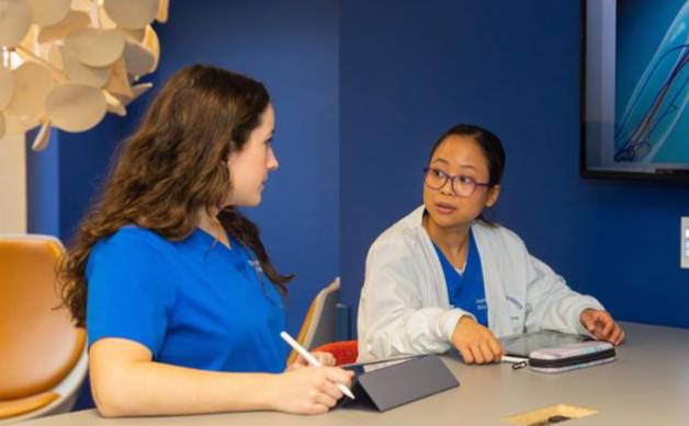 Two nursing students sit at a table, engaged in discussion. 