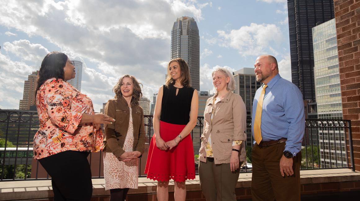 Five people standing on a terrace overlooking the city.