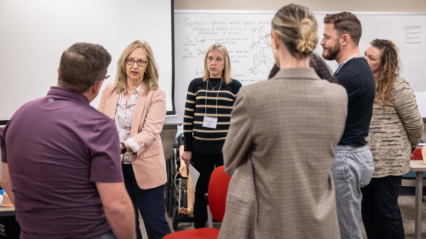 Group of nursing students and a professor talking in a classroom.
